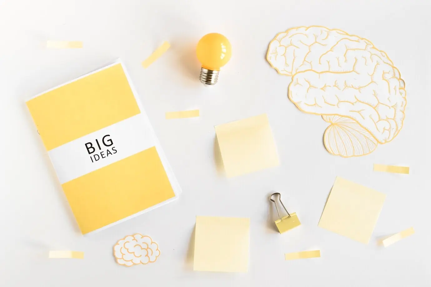 Diario de grandes ideas, bombilla, cerebro y artículos de papelería sobre fondo blanco.